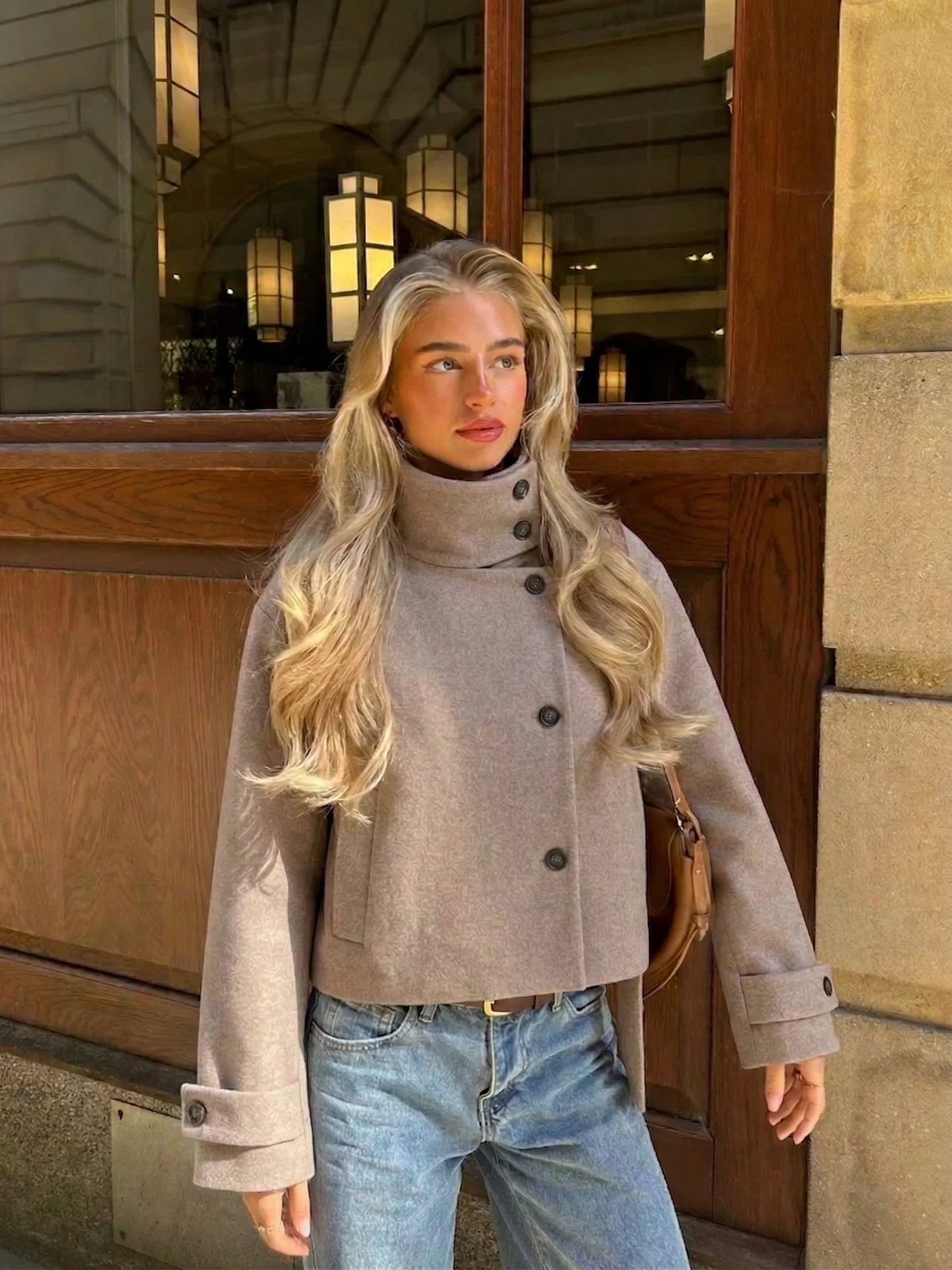 Kurze graue Damenjacke zu Jeans, Streetstyle-Aufnahme vor einer Hausfassade