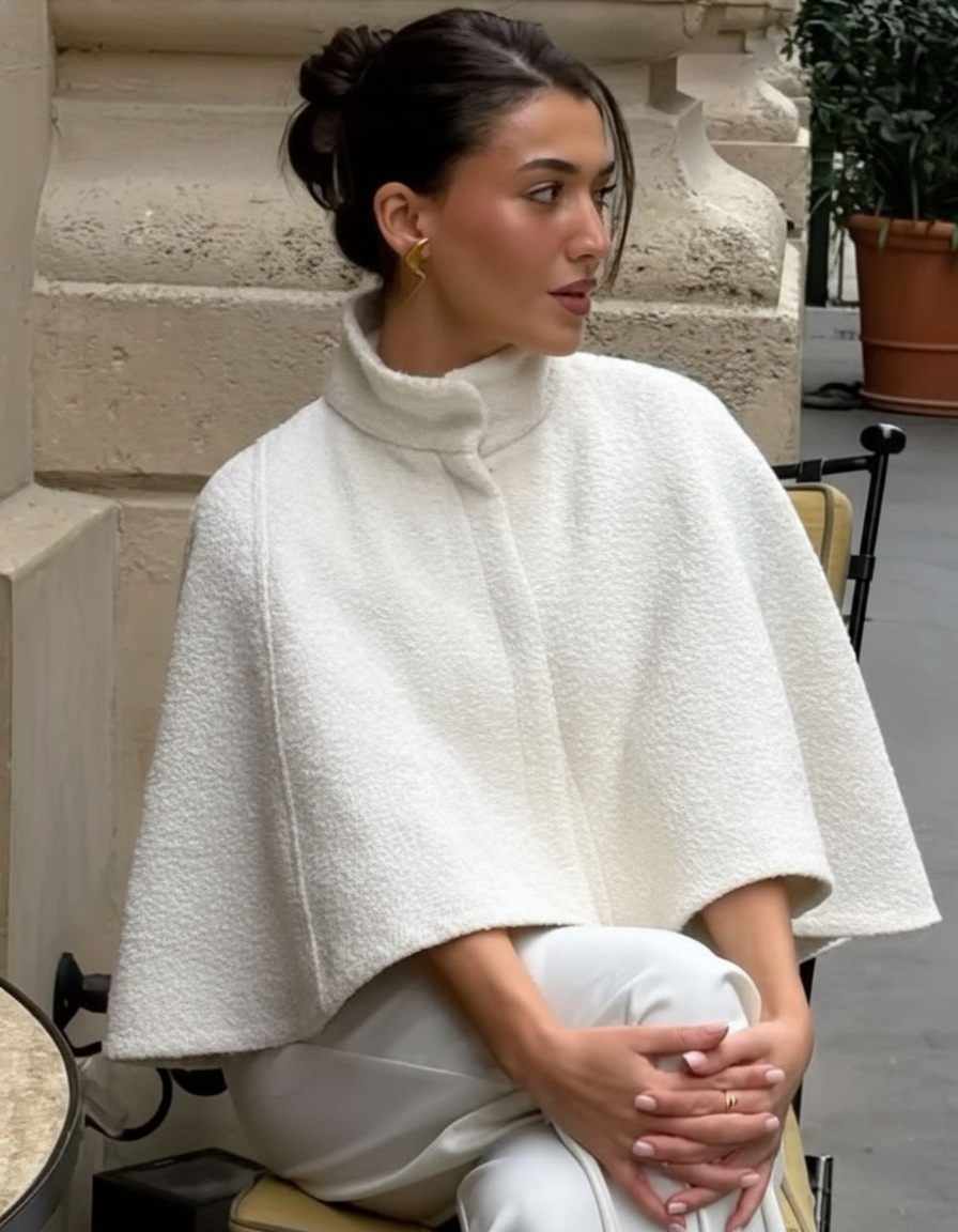 Trägerin der weißen Cape Jacke sitzt an einem Tisch im Freien