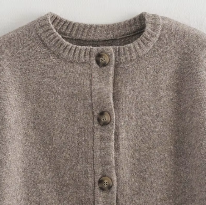 Detailaufnahme des Rundhalsausschnitts und der Knöpfe am grauen Strickcape